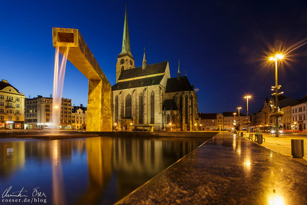 Beleuchtete St.-Bartholomäus-Kathedrale und ein goldener Brunnen auf dem Hauptplatz in Pilsen