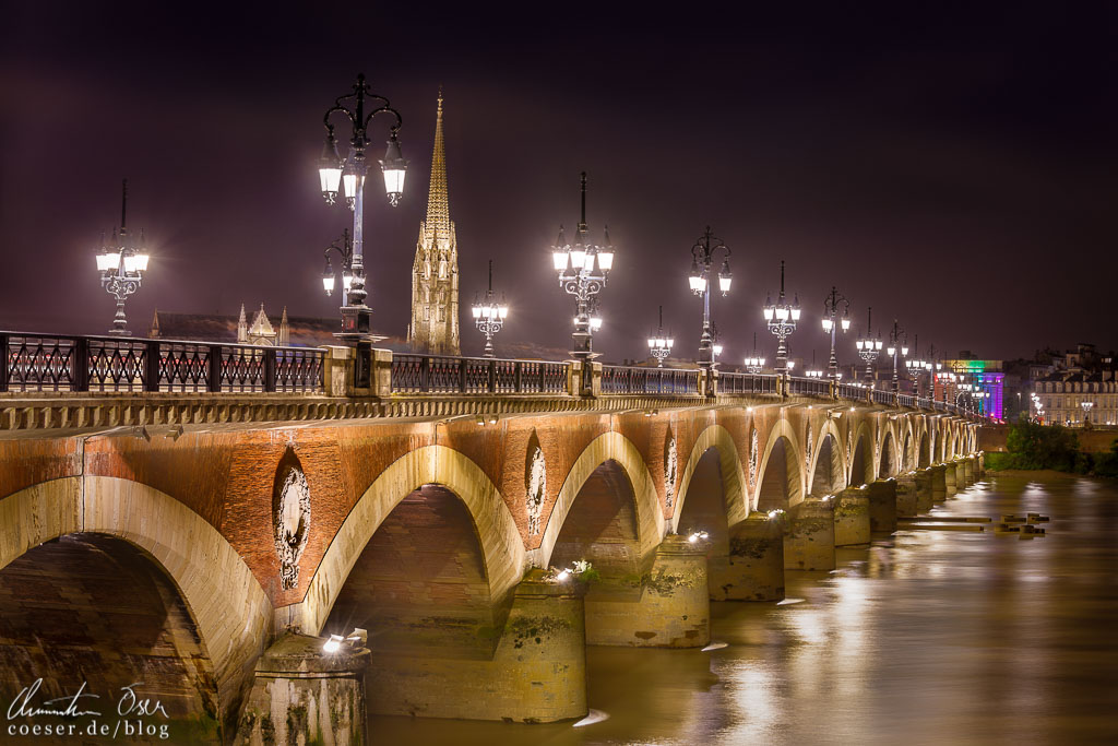 Die beleuchtete Brücke Pont de Pierre, dahinter der Glockenturm der Basilika Saint Michel in Bordeaux