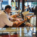 Ein Verkäufer schneidet Schinken (Jamón) in der Markthalle San Miguel (Mercado San Miguel) in Madrid