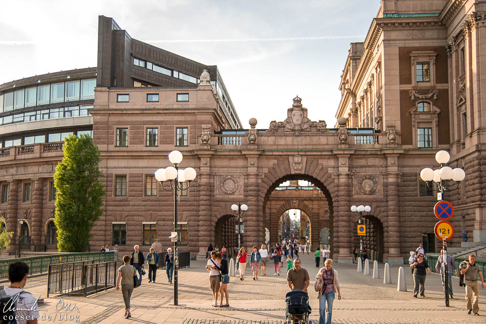 Spaziergänger auf der Straße Riksgatan mit Blick auf den bogenförmigen Durchgang des Reichstags (Riksdagshuset) in Stockholm
