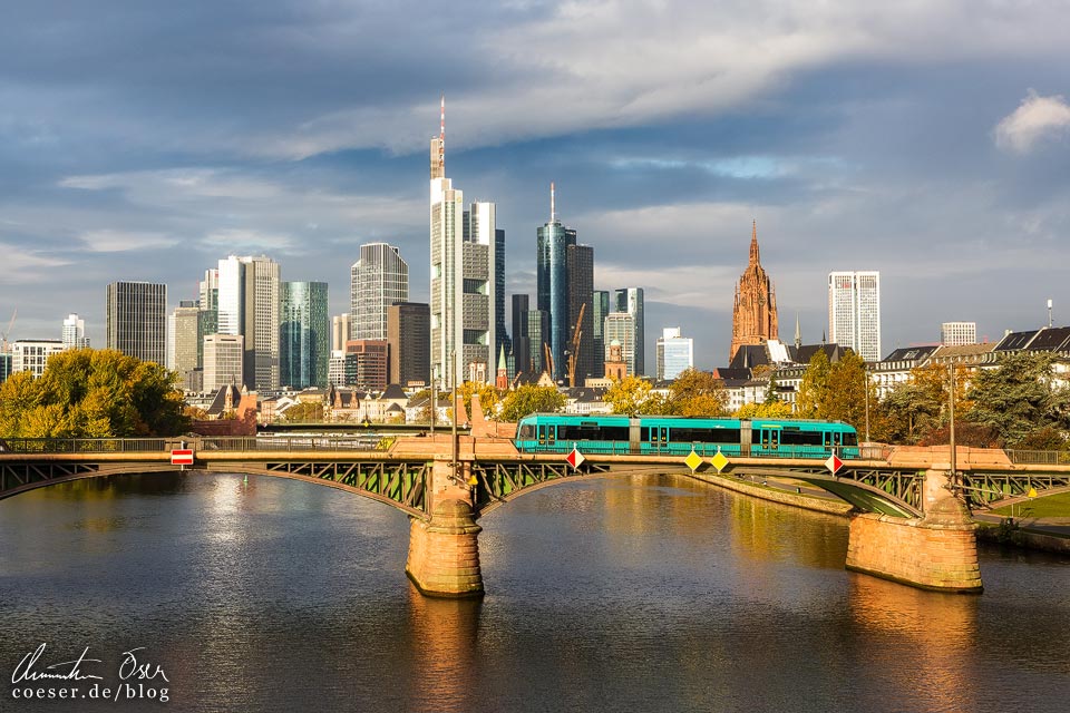Frankfurter Skyline im Sonnenaufgang, im Vordergrund eine Straßenbahn auf der Ignatz-Bubis-Brücke