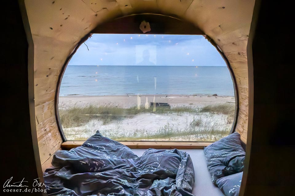 Blick aus einem Holzfass von Kempings Saulesmājas auf den Strand von Kap Kolka, Lettland