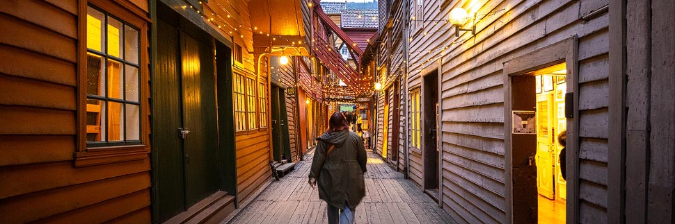 Frau in einem Durchgang zwischen den historischen Holzhäusern im Hanseviertel Bryggen in Bergen, Norwegen