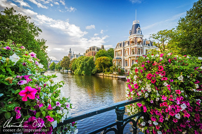 Das Gebäude Weteringschans 24 zwischen Blumen, Blick von der Museumsbrug in Amsterdam, Niederlande.