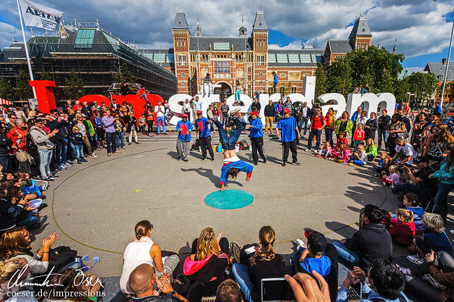 Künstler tanzen vor dem "I Amsterdam"-Logo und dem Rijksmuseum (Reichsmuseum) in Amsterdam, Niederlande.