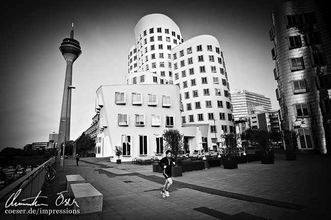 Ein Jogger läuft an den Gehry-Gebäuden und dem Rheinturm im Medienhafen vorbei in Düsseldorf, Deutschland.