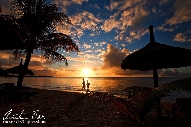 Silhouetten zweier Menschen am Strand von Trou aux biches während eines Sonnenuntergangs in Mauritius.