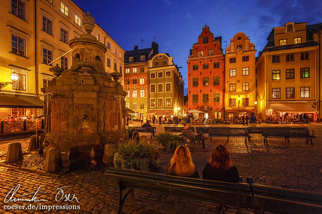 Menschen genießen auf dem bunt beleuchteten Stortorget-Platz einen lauen Sommerabend in Stockholm, Schweden.