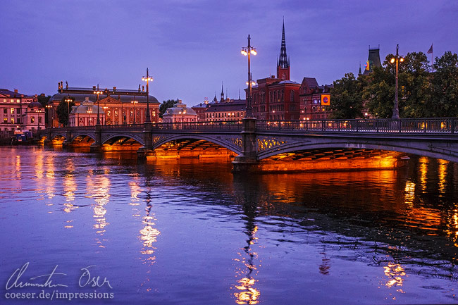 Die beleuchtete Vasabron-Brücke, die Insel Riddarholmen und die Kirche Riddarholmskyrkan in Stockholm, Schweden.