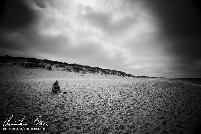 Eine Frau sitzt an einem Strand während ein Sturm aufzieht auf der Insel Sylt, Deutschland.