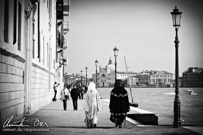 Zwei verkleidete Leute gehen an einem Kai entlang in Venedig, Italien.